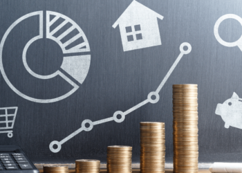 A bar graph made of stacked coins increases in height from left to right in front of a chalkboard. The chalkboard displays icons representing personal finance like a pie chart, house, magnifying glass, shopping cart, and piggy bank, along with a line graph showing an upward trend. A calculator is on the left. | ZIIMP