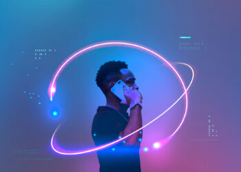 A person holds a smartphone to their ear, standing against a futuristic blue and purple backdrop, reminiscent of Ziimp.com Tech Trends 2025. Neon light trails encircle them, creating a dynamic, techno-inspired atmosphere as digital patterns and data symbols adorn the scene. | ZIIMP