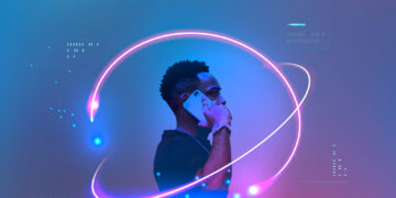 A person holds a smartphone to their ear, standing against a futuristic blue and purple backdrop, reminiscent of Ziimp.com Tech Trends 2025. Neon light trails encircle them, creating a dynamic, techno-inspired atmosphere as digital patterns and data symbols adorn the scene. | ZIIMP