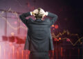 A person in a suit stands with hands on head, facing a large digital screen with declining financial graphs and red trends, symbolizing the challenge of overcoming emotional investing and staying rational in volatile markets. | ZIIMP