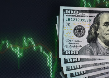 A stack of 100-dollar bills lies in the lower right corner beside a digital screen showing a green, declining stock market graph on a dark background, highlighting the potential benefits of Dollar-Cost Averaging during downturns. | ZIIMP